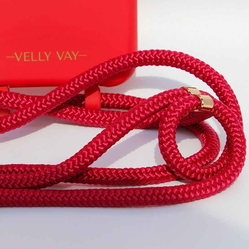 May include: A red phone case with a red rope strap and gold hardware. The case has the text "VELLY VAY" printed on it.