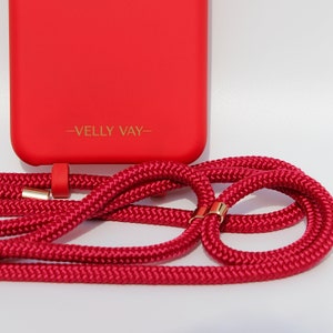 May include: A red phone case with a gold logo that says "VELLY VAY" and a red phone strap with gold accents.