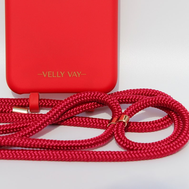 May include: A red phone case with a gold logo that says "VELLY VAY" and a red phone strap with gold accents.