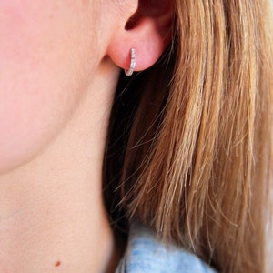 Peut inclure: Gros plan sur une oreille portant une petite boucle d'oreille en argent avec de minuscules pierres claires serties dans le métal.