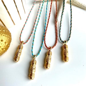 Peut inclure: Quatre colliers avec pendentifs en or aux motifs complexes, chacun sur un cordon de couleur différente : corail, turquoise, bleu marine et crème.