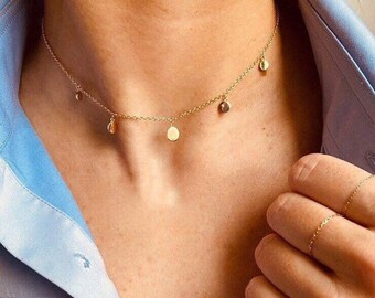 May include: A gold chain necklace with multiple small round charms hanging from it. The necklace is worn by a person with a light blue shirt.