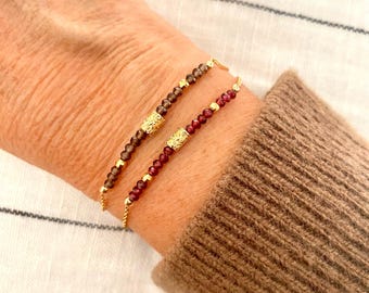 May include: Two delicate bracelets with gold accents and small gemstone beads. One bracelet features brown beads and the other features red beads.