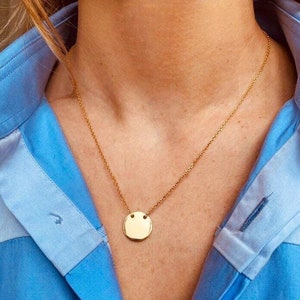 May include: A gold chain necklace with a round pendant. The pendant is smooth and has a slightly textured surface.