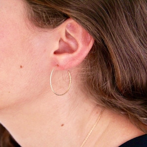 Peut inclure: Gros plan sur une oreille portant une fine boucle d'oreille en or. La boucle d'oreille est simple et délicate, avec une finition lisse et polie.