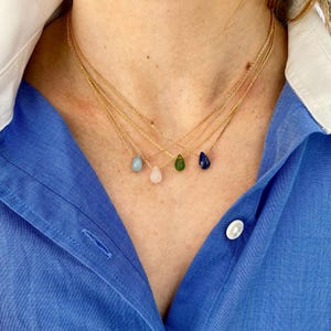 Peut inclure: Quatre colliers en or avec des pendentifs en pierres précieuses en forme de goutte. Les pendentifs sont bleus, verts, roses et bleu clair.