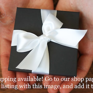 May include: A black gift box with a white satin ribbon tied in a bow. The box is sitting in the palm of a person's hand.