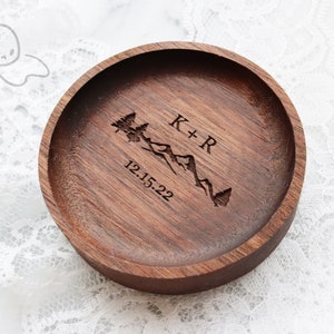 May include: A wooden ring dish with a mountain and tree design engraved on the top. The dish is personalised with the initials "K+R" and the date "12.15.22".