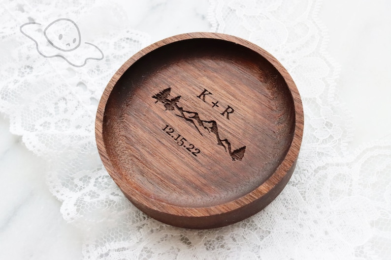 May include: A wooden ring dish with a mountain and tree design engraved on the top. The dish is personalised with the initials "K+R" and the date "12.15.22".