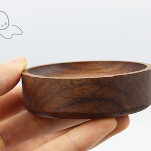 May include: A small, round, wooden bowl with a dark brown color. The bowl is made of walnut wood and has a smooth, polished finish.