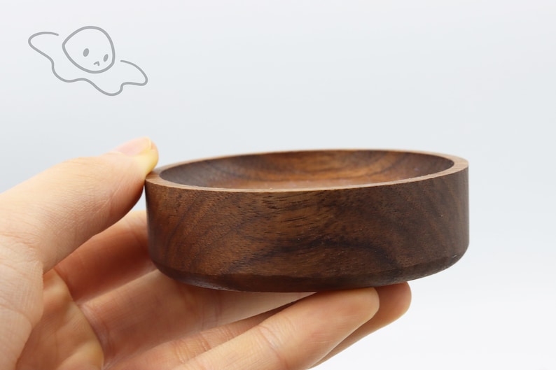 May include: A small, round, wooden bowl with a dark brown color. The bowl is made of walnut wood and has a smooth, polished finish.