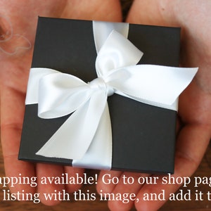 May include: A black gift box with a white satin ribbon tied in a bow. The box is sitting in the palm of a person's hand.