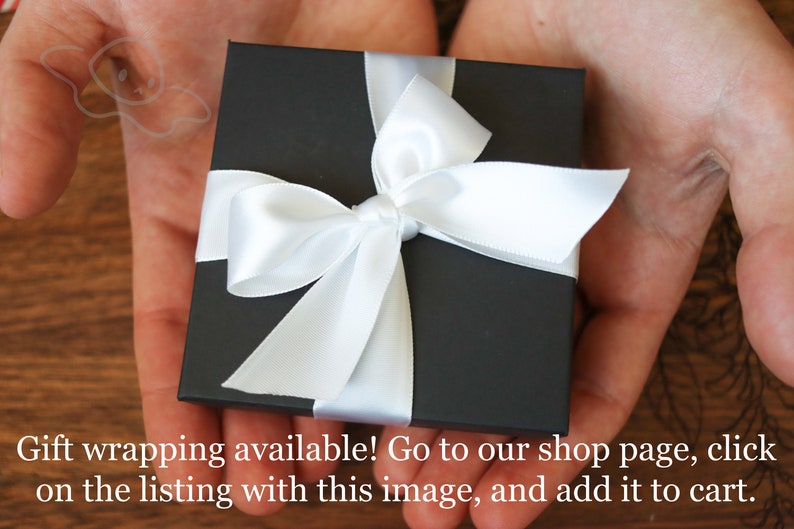 May include: A black gift box with a white satin ribbon tied in a bow. The box is sitting in the palm of a person's hand.