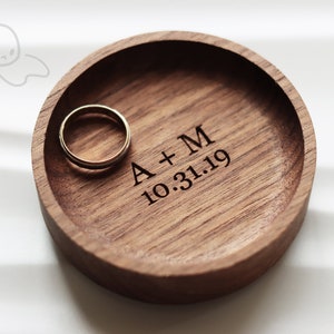 May include: A wooden ring dish with a ring inside. The dish is engraved with "A + M 10.31.19".