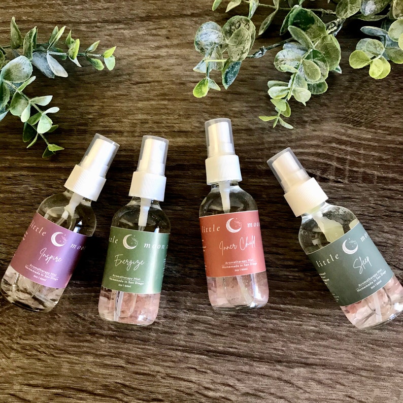 Op de afbeelding: Vier glazen flessen met witte spuitkoppen en groen-witte etiketten. De etiketten hebben de tekst "little moon" en de namen van de geuren: "Jasper", "Energize", "Inner Child" en "Sleep".