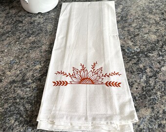 May include: White kitchen towel with a brown sunflower design and arrows on the bottom.