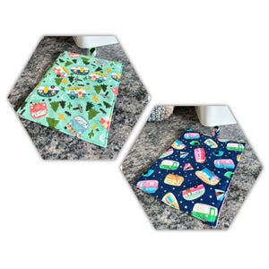 May include: Two quilted pot holders with camping-themed patterns. One is light green with camper vans, trees, and other camping elements. The other is navy blue with colorful camper vans and geometric shapes. Both have a hanging loop.