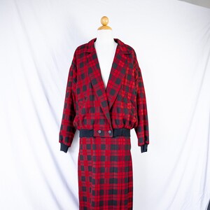 May include: A red and black plaid skirt suit with a double-breasted jacket. The jacket has a black ribbed waistband and the skirt has pleats.