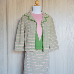 May include: A pink and green striped knit skirt suit with a matching jacket. The jacket has a green trim around the collar and cuffs. The skirt is knee-length.