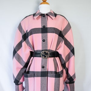 May include: A pink and black plaid oversized shirt with a black leather belt with a gold buckle. The shirt has a collared neckline and long sleeves.