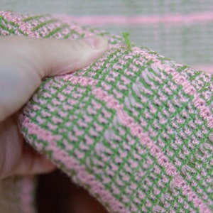 May include: Close-up of a pink and green striped fabric with a loose thread hanging from the edge.