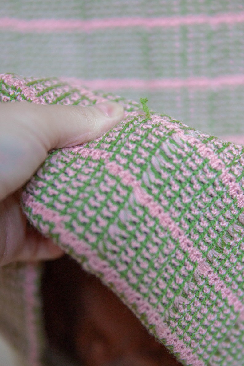 May include: Close-up of a pink and green striped fabric with a loose thread hanging from the edge.