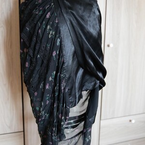 Peut inclure: Robe noire avec imprim&eacute; floral et d&eacute;tails en dentelle. La robe pr&eacute;sente un design drap&eacute; avec un tissu satin&eacute; d'un c&ocirc;t&eacute; et un tissu &agrave; motifs floraux de l'autre. Un d&eacute;tail de bouton est visible.