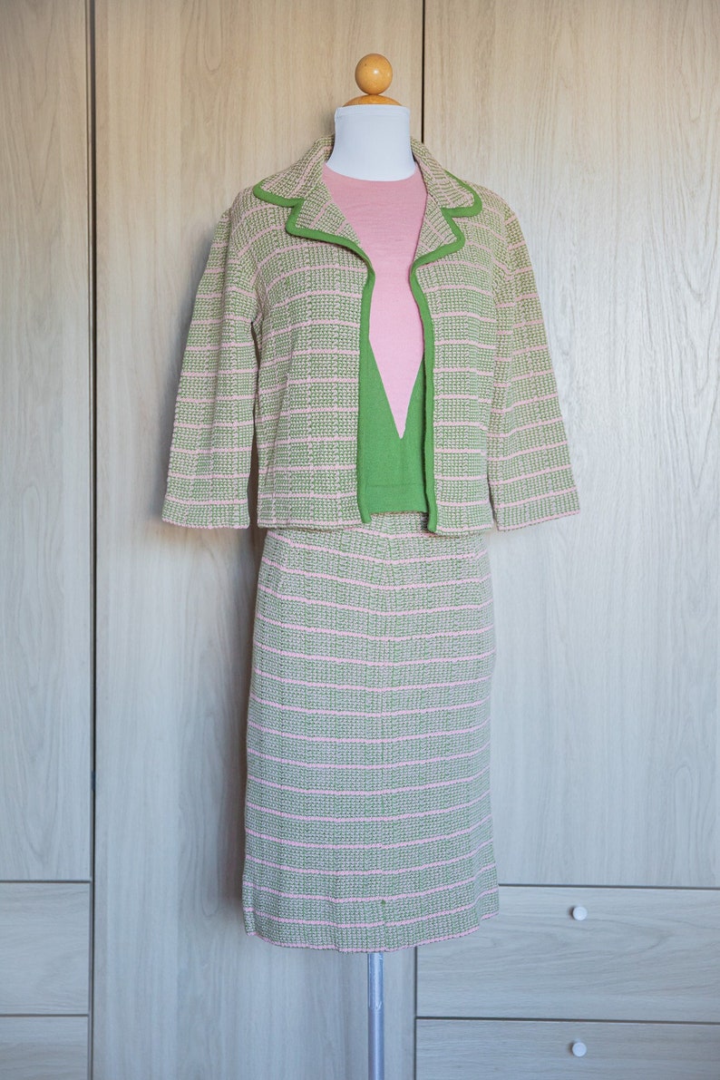 May include: A pink and green striped knit skirt suit with a matching jacket. The jacket has a green trim around the collar and cuffs. The skirt is knee-length.