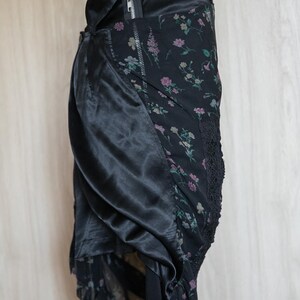 Peut inclure: Jupe noire avec un motif floral et un panneau en satin. La jupe est dot&eacute;e d'une fermeture &eacute;clair et d'une bordure en dentelle. Le motif floral comprend des fleurs roses et blanches sur fond noir. La jupe a un design superpos&eacute;.
