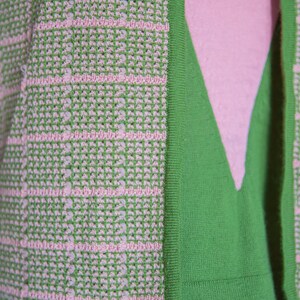 May include: A green and pink knitted cardigan with a textured pattern. The cardigan has a V-neck and a ribbed trim.