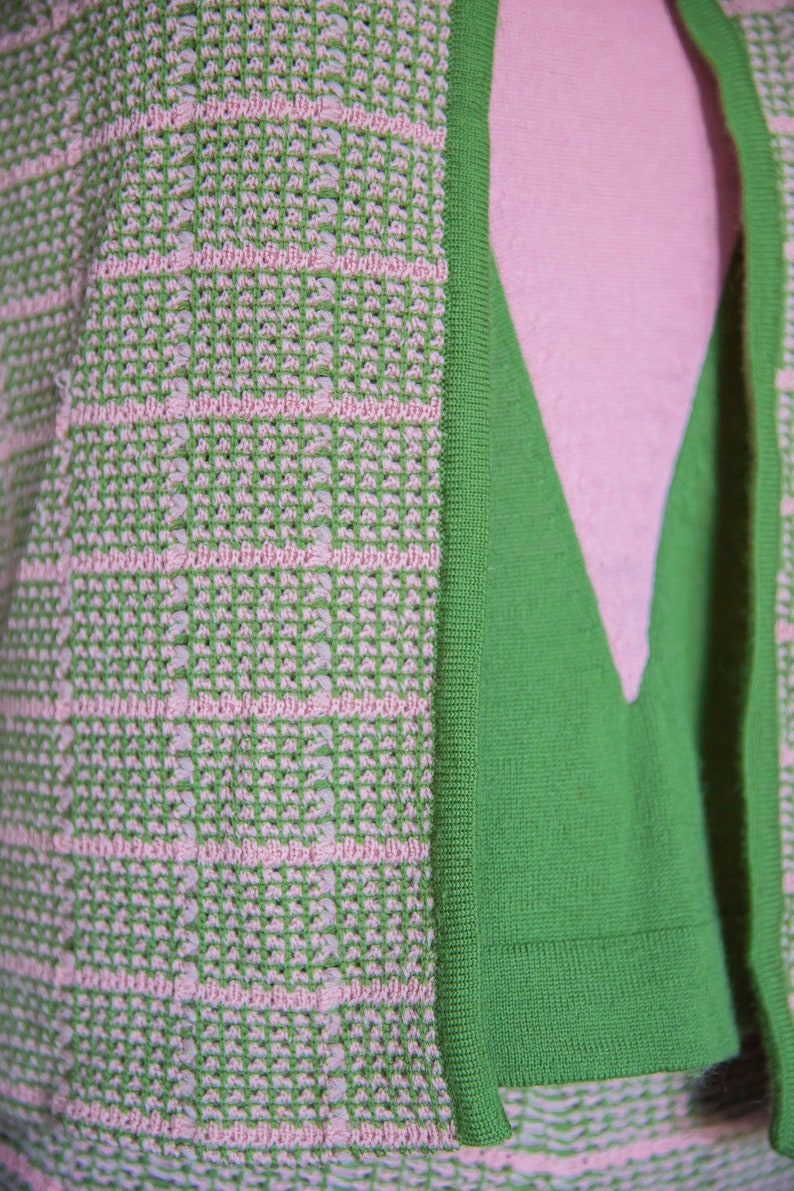 May include: A green and pink knitted cardigan with a textured pattern. The cardigan has a V-neck and a ribbed trim.