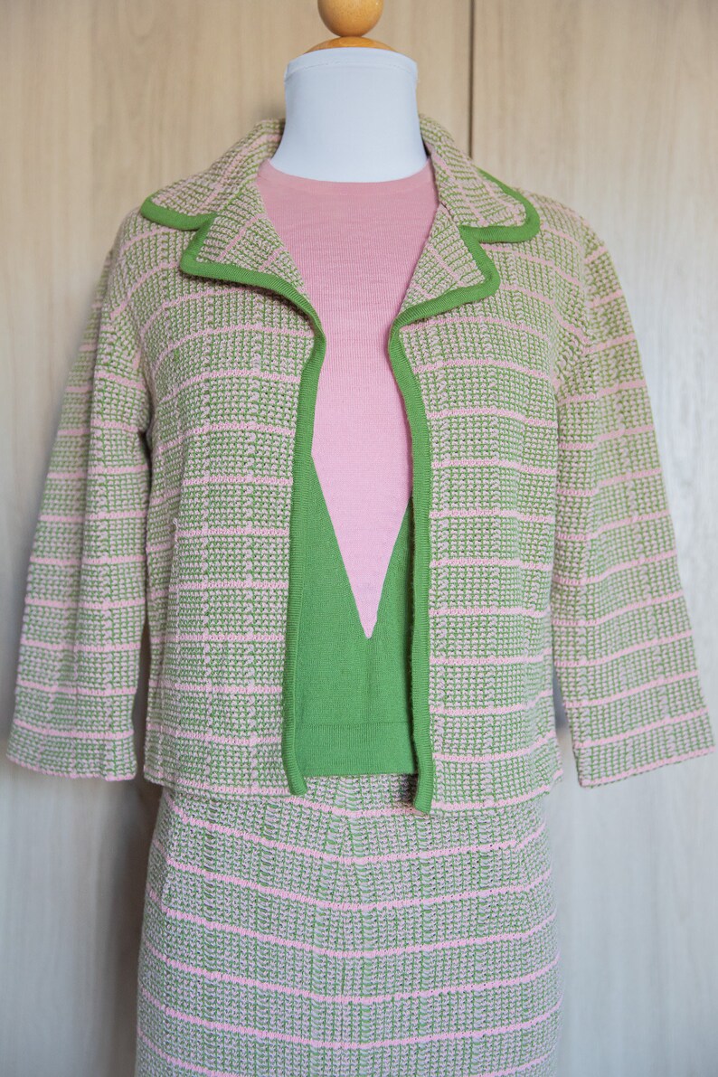 May include: A pink and green knit skirt suit with a matching top. The jacket has a green trim and the skirt and top have a pink and green checkered pattern.