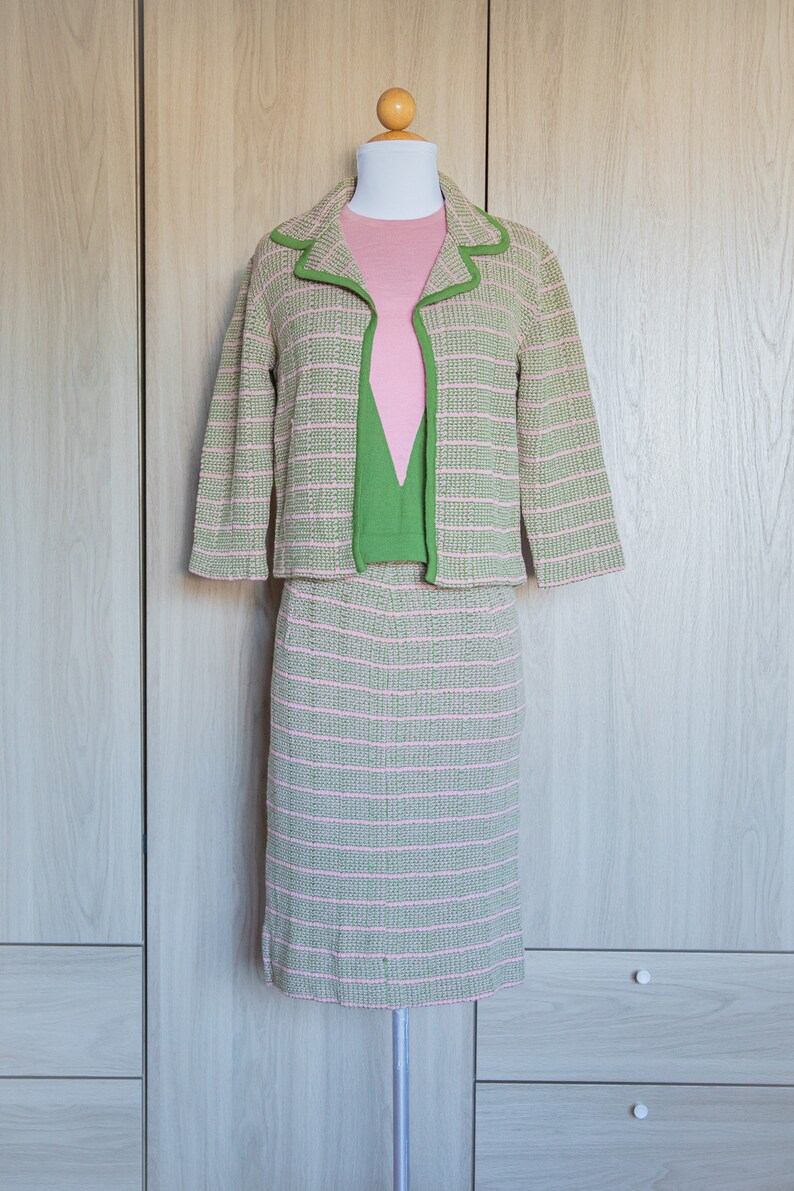 May include: A pink and green striped knit suit jacket and skirt set on a mannequin. The jacket has a green trim and the skirt is knee-length.