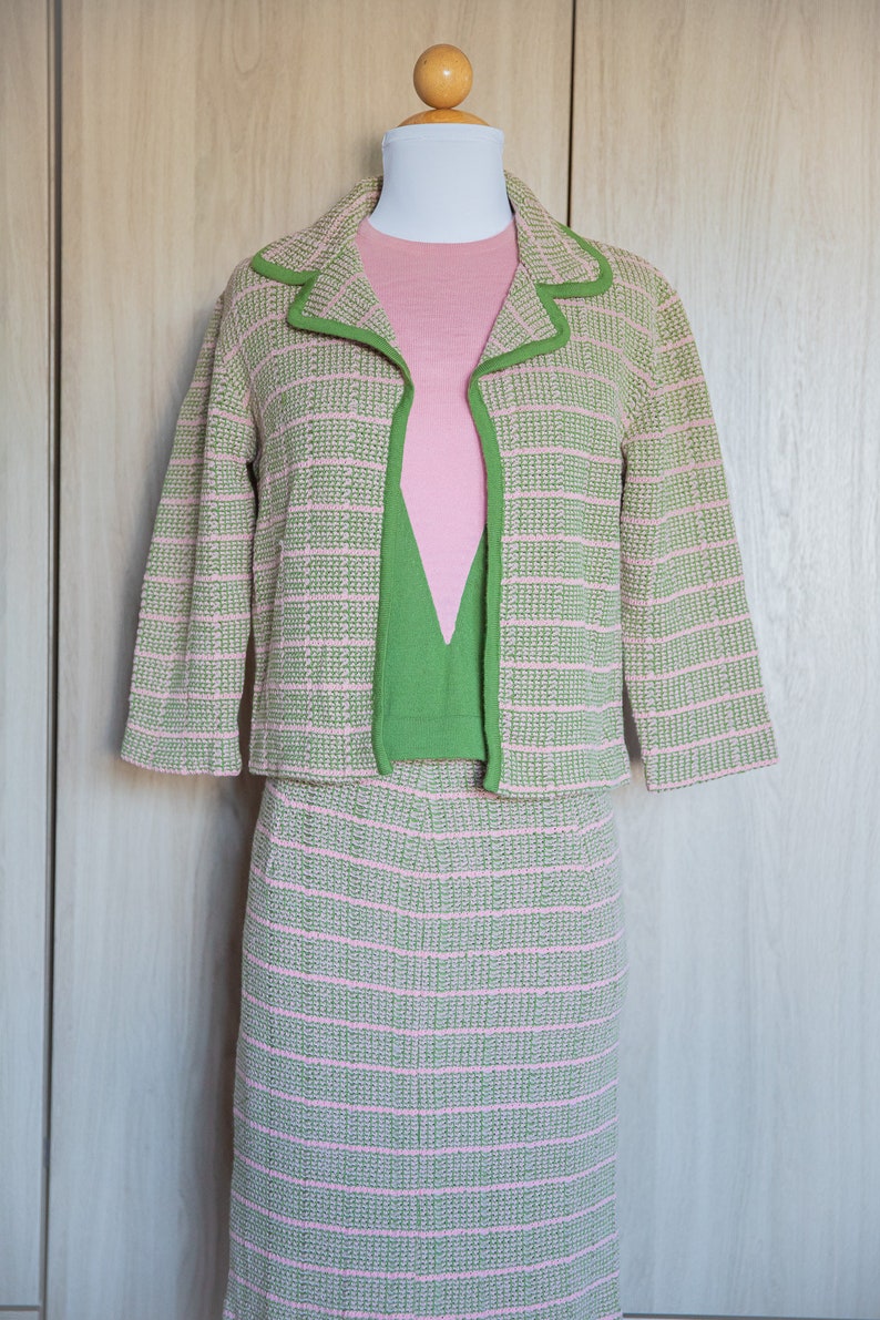 May include: A pink and green striped knit suit with a matching skirt and jacket. The jacket has a green trim around the collar and cuffs.
