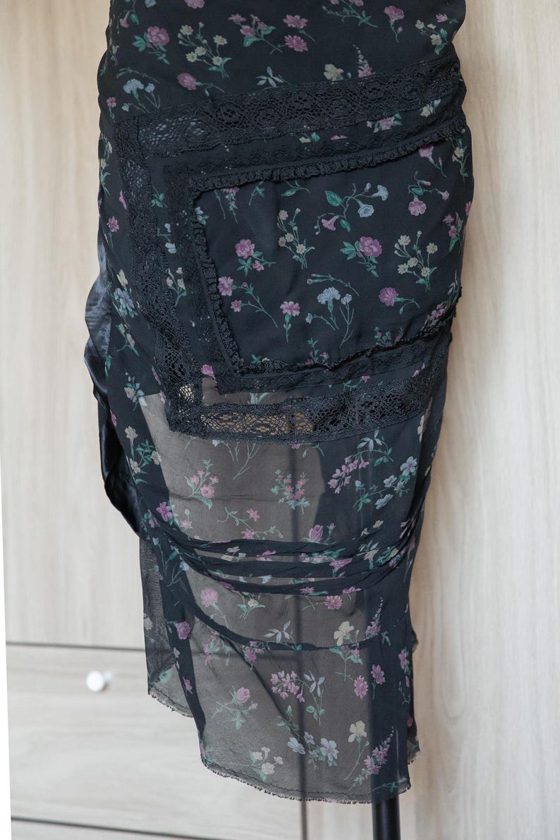 Peut inclure: Jupe noire &agrave; imprim&eacute; floral avec superposition transparente. Le motif floral pr&eacute;sente des fleurs roses, violettes et bleues. Des bordures en dentelle noire ornent les bords. La jupe est faite d'un tissu l&eacute;ger et fluide.