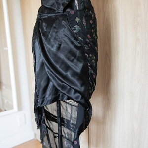 Peut inclure: Jupe en satin noir avec un design drap&eacute;. La jupe pr&eacute;sente un panneau &agrave; imprim&eacute; floral et une fermeture &eacute;clair. La jupe est pr&eacute;sent&eacute;e sur un mannequin.