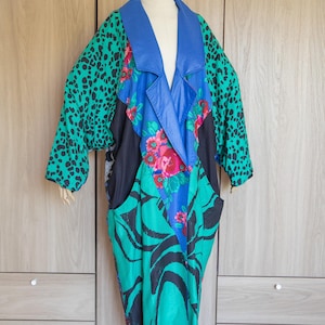 May include: A vibrant, patterned coat with a blue collar and sleeves featuring a green leopard print. The coat's body showcases a mix of floral, black, and green zebra-like patterns, creating a bold, artistic statement.