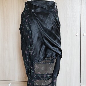Peut inclure: Jupe noire avec un imprim&eacute; floral et un drap&eacute; en satin. La jupe pr&eacute;sente une fermeture boutonn&eacute;e et un design superpos&eacute;, mettant en valeur un m&eacute;lange de textures et de motifs. La jupe est pr&eacute;sent&eacute;e sur un mannequin.