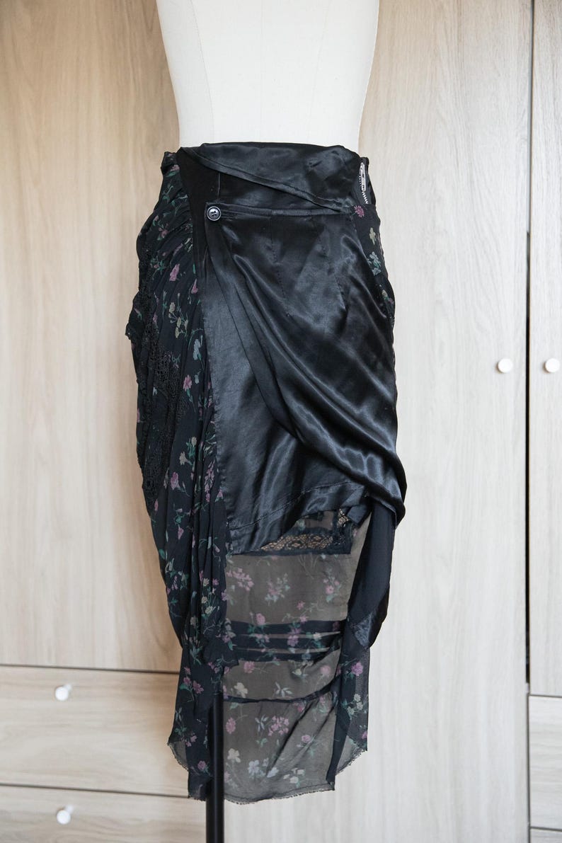Peut inclure: Jupe noire avec un imprim&eacute; floral et un drap&eacute; en satin. La jupe pr&eacute;sente une fermeture boutonn&eacute;e et un design superpos&eacute;, mettant en valeur un m&eacute;lange de textures et de motifs. La jupe est pr&eacute;sent&eacute;e sur un mannequin.
