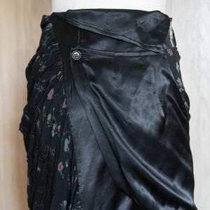 Peut inclure: Jupe noire au design unique. La jupe pr&eacute;sente un rev&ecirc;tement en satin qui recouvre un tissu &agrave; motifs floraux. Une fermeture &agrave; bouton et &agrave; glissi&egrave;re est visible. Le tissu floral a une bordure en dentelle.