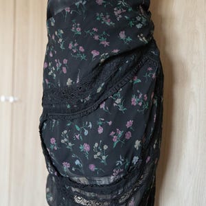 Peut inclure: Jupe noire &agrave; imprim&eacute; floral avec bordure en dentelle. La jupe pr&eacute;sente un motif d&eacute;licat de petites fleurs roses et vertes sur fond noir. La jupe est faite d'un tissu l&eacute;ger et a un design superpos&eacute;.