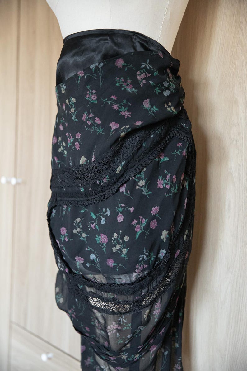 Peut inclure: Jupe noire &agrave; imprim&eacute; floral avec bordure en dentelle. La jupe pr&eacute;sente un motif d&eacute;licat de petites fleurs roses et vertes sur fond noir. La jupe est faite d'un tissu l&eacute;ger et a un design superpos&eacute;.