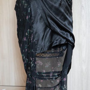 Peut inclure: Jupe noire avec imprim&eacute; floral et d&eacute;tails en dentelle. La jupe pr&eacute;sente un rev&ecirc;tement en satin drap&eacute; et une sous-couche florale transparente. Le motif floral comprend des fleurs roses et violettes sur fond sombre. Fermeture boutonn&eacute;e.