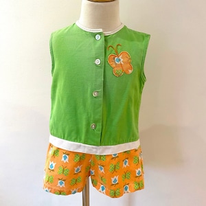 May include: A green sleeveless jumpsuit with a white trim and orange and blue butterfly print shorts. The top has a button closure and a small butterfly applique.