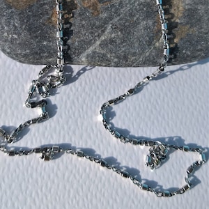 Peut inclure: Un collier en chaîne argent avec un design de chaîne à maillons carrés. La chaîne est composée de petits maillons carrés.