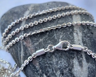 Puede incluir: Un collar de cadena de plata con un cierre de langosta. La cadena está hecha de pequeños eslabones redondos y está sobre una roca gris.