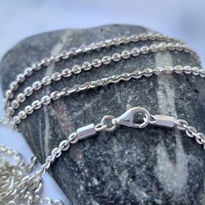 Puede incluir: Un collar de cadena de plata con un cierre de langosta. La cadena está hecha de pequeños eslabones redondos y está sobre una roca gris.
