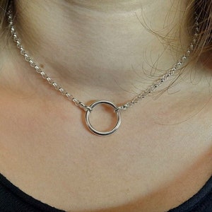 Könnte beinhalten: Eine silberne Ketten-Choker-Halskette mit einem großen silbernen Ring-Anhänger.