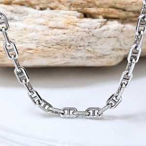 May include: A silver-toned metal chain necklace featuring a series of elongated oval links, each reinforced with a central horizontal bar. The polished links are interconnected to form a continuous, uniform pattern throughout the entire length of the chain.