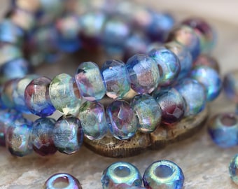 May include: Close-up of iridescent glass beads in shades of blue, purple, and green. The beads are faceted and strung together, with some loose beads scattered around. The beads are for jewelry making.